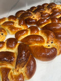 Several braided bread loaves with glossy golden-brown crusts arranged on a white surface.